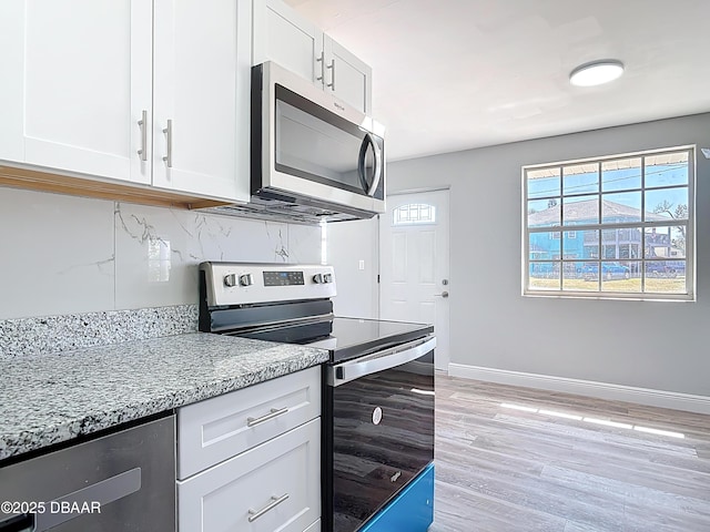 kitchen featuring tasteful backsplash, white cabinetry, appliances with stainless steel finishes, baseboards, and light stone countertops