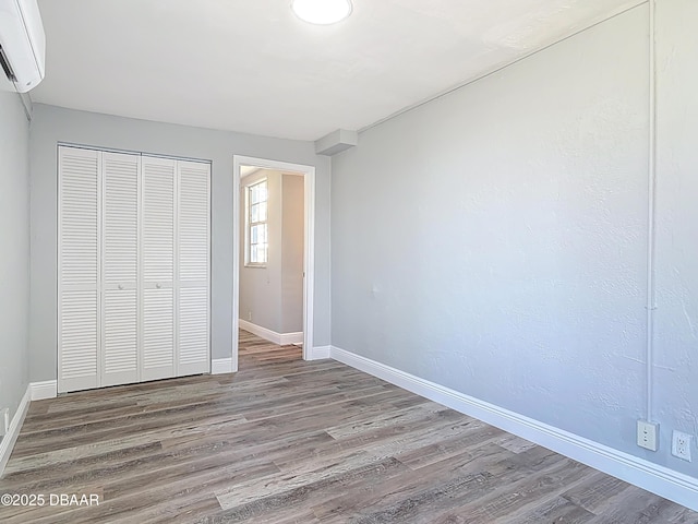 unfurnished bedroom with a closet, baseboards, an AC wall unit, and wood finished floors