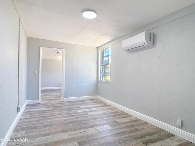 empty room featuring a wall mounted air conditioner, baseboards, wood finished floors, and a textured wall