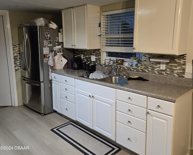 kitchen with sink, white cabinetry, backsplash, and stainless steel refrigerator