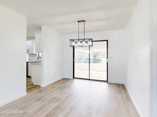 unfurnished dining area with an inviting chandelier and light wood-type flooring