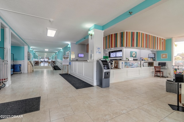 interior space featuring a textured ceiling, light tile patterned floors, beam ceiling, and white cabinets