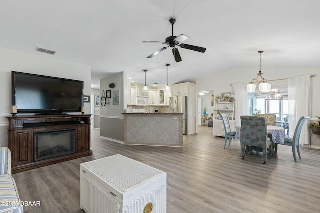 living room with lofted ceiling, ceiling fan with notable chandelier, and wood-type flooring