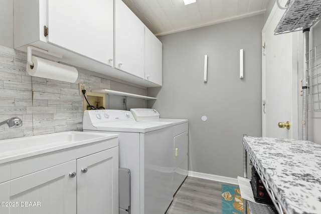 clothes washing area with independent washer and dryer, light wood-type flooring, cabinets, and sink