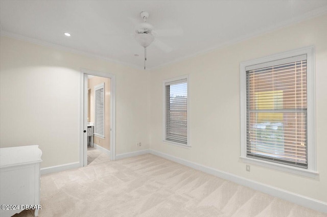 empty room featuring a wealth of natural light, light colored carpet, ceiling fan, and crown molding