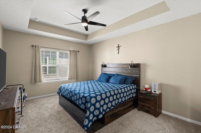 carpeted bedroom featuring a textured ceiling, ceiling fan, and a raised ceiling