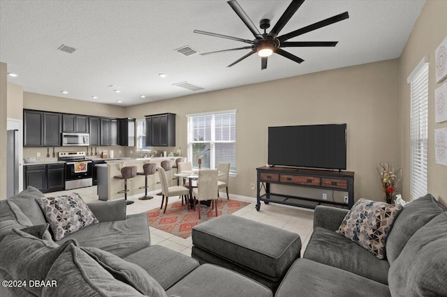 living room with ceiling fan, a textured ceiling, and light tile patterned floors