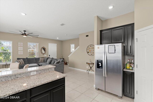 kitchen featuring light tile patterned flooring, light stone counters, stainless steel refrigerator with ice dispenser, ceiling fan, and a textured ceiling