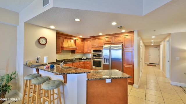kitchen with tasteful backsplash, stainless steel appliances, dark stone countertops, visible vents, and a peninsula