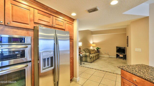 kitchen featuring visible vents, appliances with stainless steel finishes, dark stone countertops, open floor plan, and light tile patterned floors