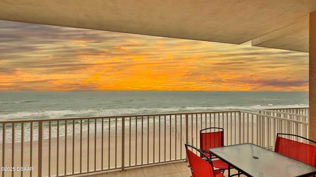 balcony with a beach view, outdoor dining space, and a water view