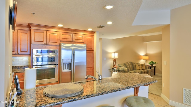 kitchen featuring backsplash, a breakfast bar area, appliances with stainless steel finishes, open floor plan, and dark stone counters