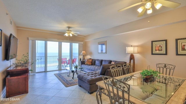living area featuring light tile patterned flooring, a water view, a textured ceiling, visible vents, and ceiling fan