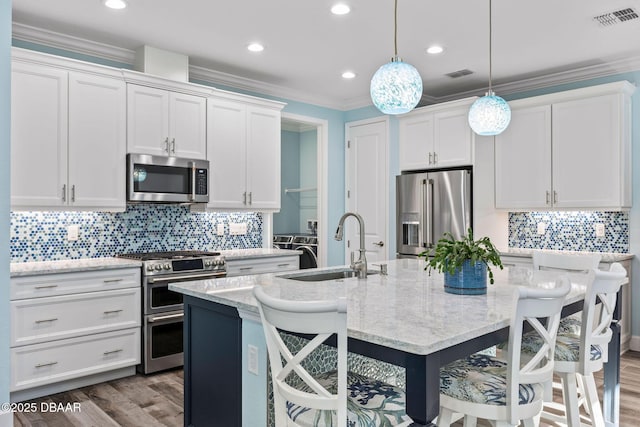 kitchen with stainless steel appliances, white cabinetry, light stone countertops, and an island with sink