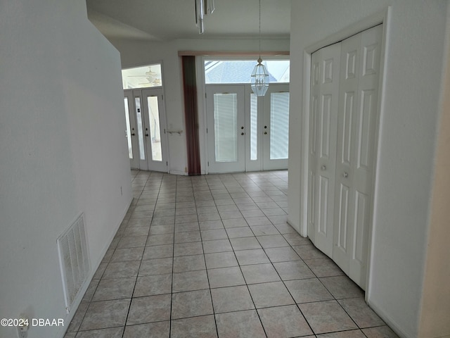 hall featuring french doors, light tile patterned flooring, and a notable chandelier