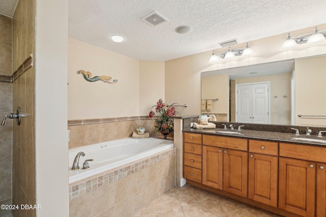 bathroom with a textured ceiling, vanity, tile patterned floors, and tiled tub