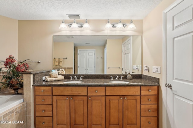 bathroom with a textured ceiling, vanity, and tiled bath