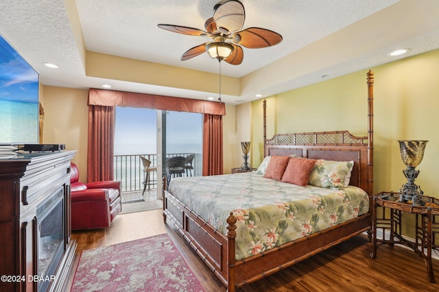 bedroom featuring a textured ceiling, access to outside, a tray ceiling, ceiling fan, and hardwood / wood-style flooring