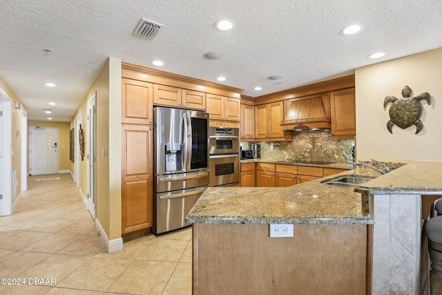 kitchen with stone counters, sink, stainless steel appliances, kitchen peninsula, and custom range hood