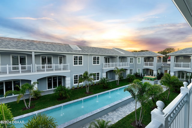 pool at dusk featuring a lawn and pool water feature