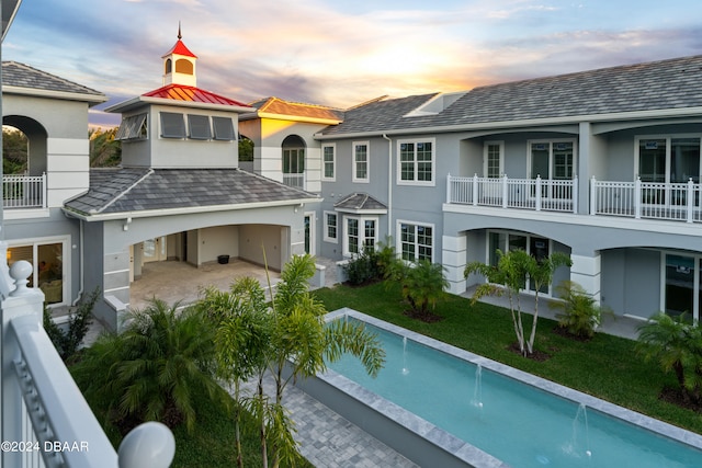 back house at dusk with a balcony, a yard, a patio, and pool water feature