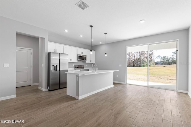 23 Weymouth Ln, Palm Coast, FL 32164 - kitchen featuring stainless steel appliances, white cabinets, wood finished floors, light countertops, and an island with sink