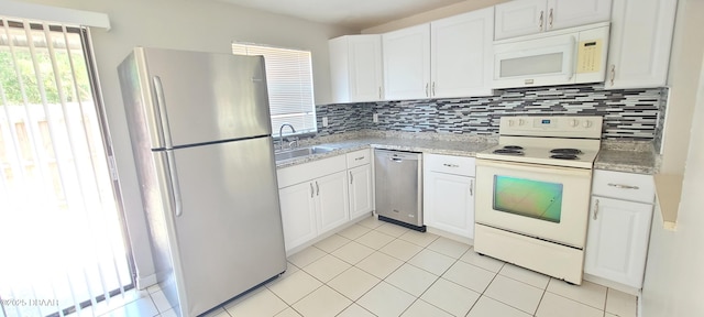 kitchen featuring a sink, stainless steel appliances, light tile patterned floors, backsplash, and white cabinets