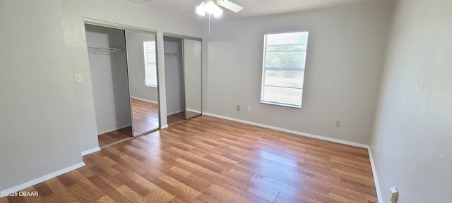 unfurnished bedroom featuring a ceiling fan, wood finished floors, multiple closets, and baseboards