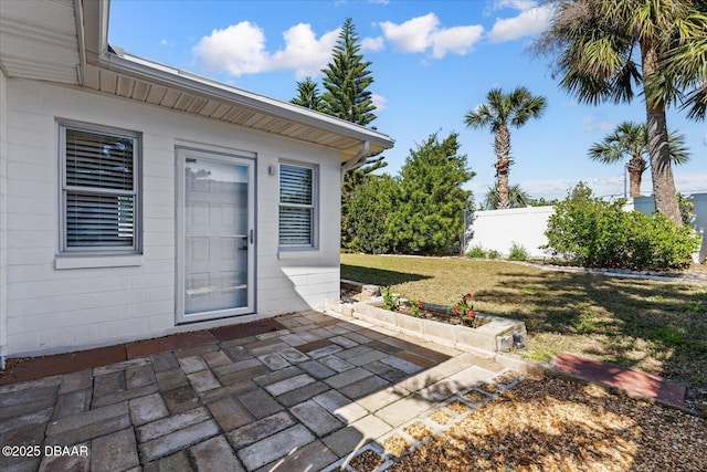 view of exterior entry with a patio, fence, and a lawn