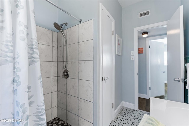 full bath featuring a tile shower, visible vents, and baseboards