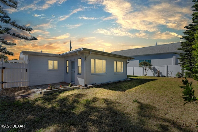 back of house at dusk featuring fence and a lawn