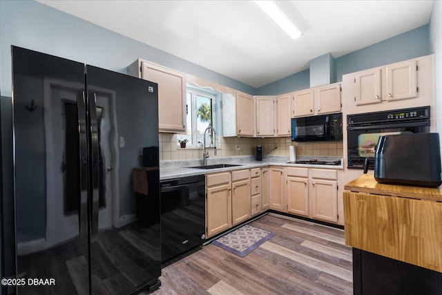 kitchen with a sink, vaulted ceiling, light countertops, backsplash, and black appliances