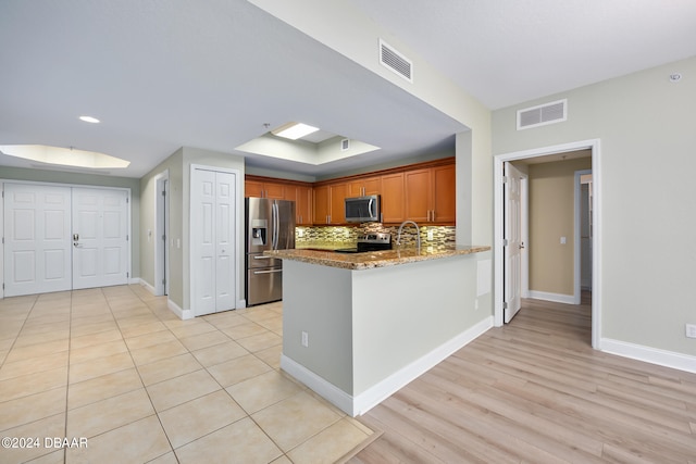 kitchen featuring sink, kitchen peninsula, stainless steel appliances, light stone countertops, and decorative backsplash