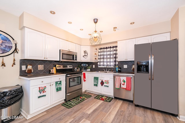 kitchen featuring appliances with stainless steel finishes, sink, pendant lighting, white cabinets, and light hardwood / wood-style floors