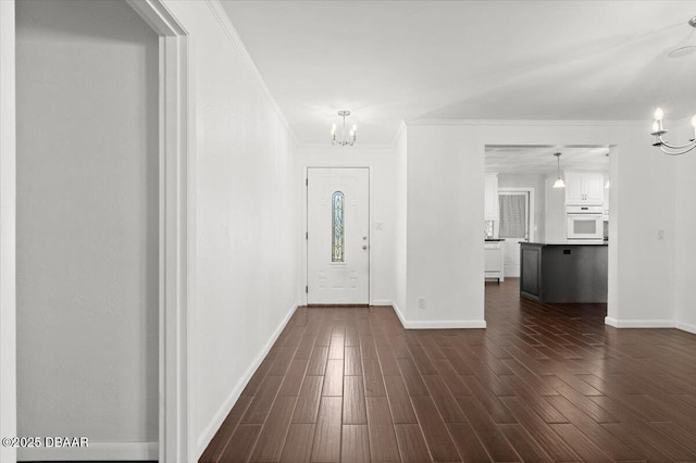 foyer entrance featuring an inviting chandelier, ornamental molding, and dark wood-type flooring