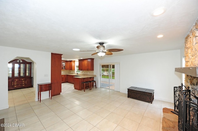 kitchen featuring kitchen peninsula, tasteful backsplash, a kitchen breakfast bar, ceiling fan, and light tile patterned flooring