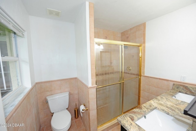 bathroom featuring toilet, vanity, tile walls, and a shower with shower door