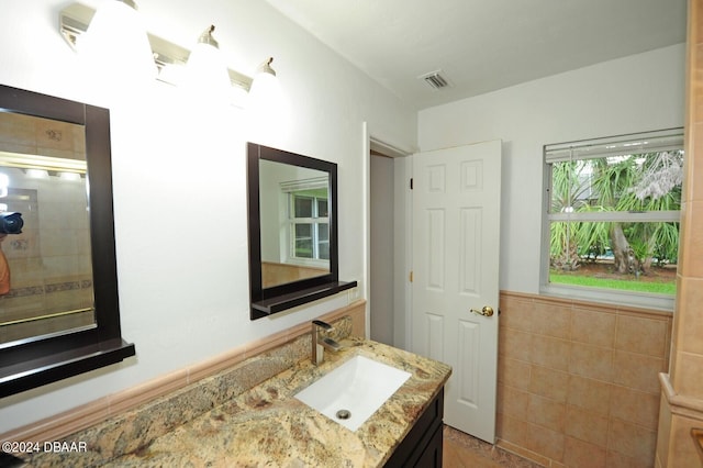 bathroom with walk in shower, vanity, and tile walls