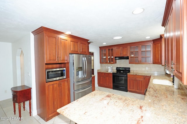 kitchen featuring stainless steel appliances, backsplash, light tile patterned floors, light stone countertops, and sink