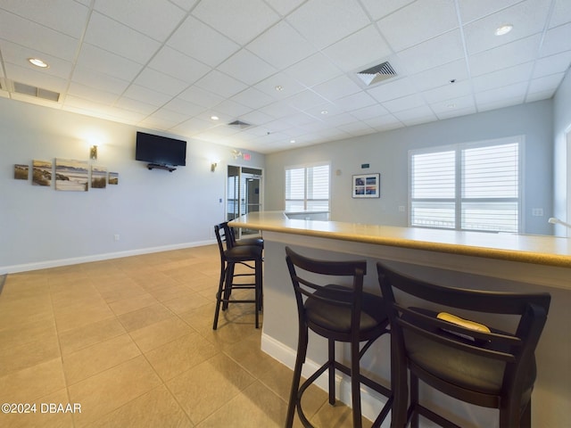 kitchen with light tile patterned flooring, a wealth of natural light, a drop ceiling, and a kitchen breakfast bar