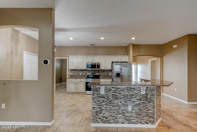 kitchen featuring light tile patterned flooring, a breakfast bar, a center island with sink, appliances with stainless steel finishes, and decorative backsplash