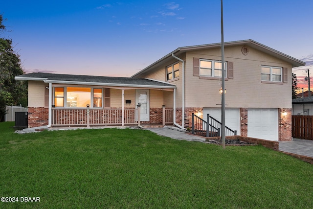 view of front of home featuring a lawn, central air condition unit, a garage, and covered porch