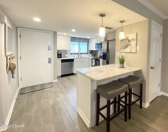 kitchen with stainless steel appliances, light hardwood / wood-style floors, white cabinets, kitchen peninsula, and pendant lighting