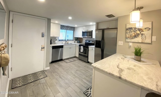 kitchen featuring stainless steel appliances, white cabinets, hanging light fixtures, sink, and light wood-type flooring