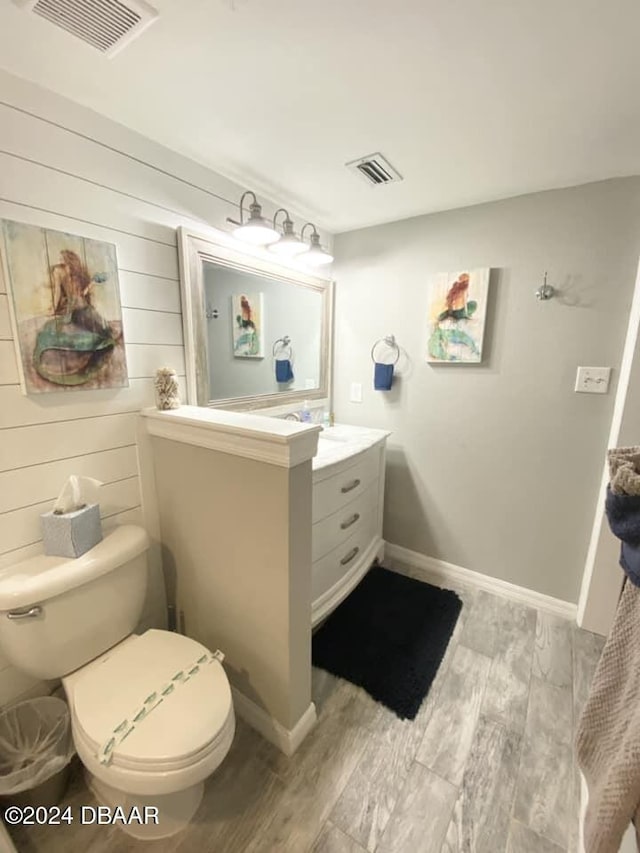 bathroom with wood walls, wood-type flooring, vanity, and toilet