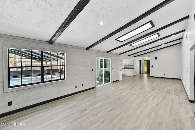 unfurnished living room with a textured ceiling, lofted ceiling with beams, light hardwood / wood-style flooring, and wood walls