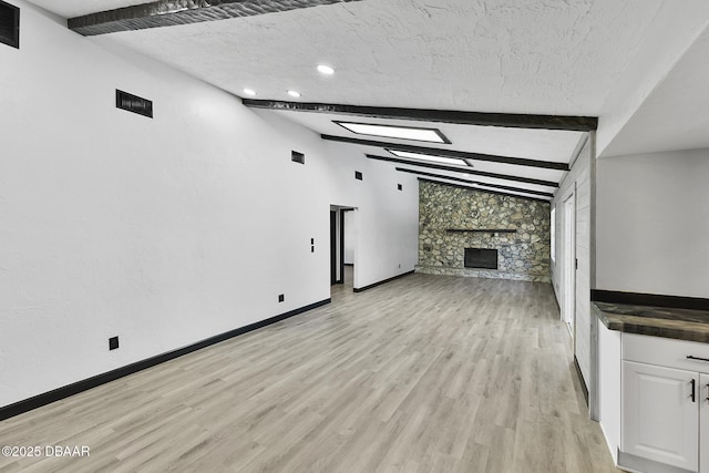 unfurnished living room featuring lofted ceiling with beams, light hardwood / wood-style floors, a stone fireplace, and a textured ceiling