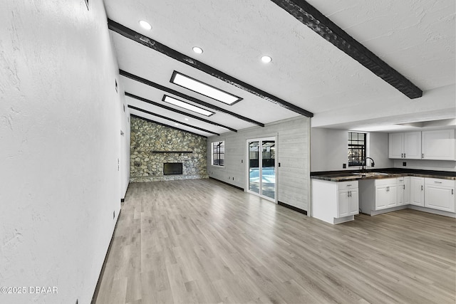 kitchen with a stone fireplace, light hardwood / wood-style flooring, lofted ceiling with beams, a textured ceiling, and white cabinets