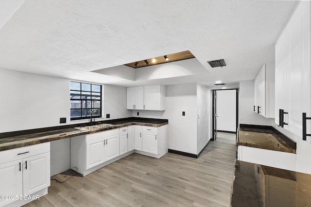 kitchen with white cabinetry, sink, a raised ceiling, light hardwood / wood-style flooring, and a textured ceiling