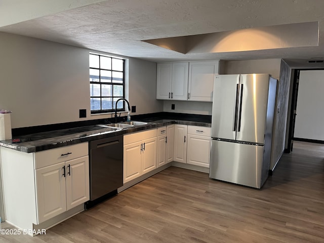 kitchen featuring sink, light wood-type flooring, black dishwasher, white cabinetry, and stainless steel refrigerator